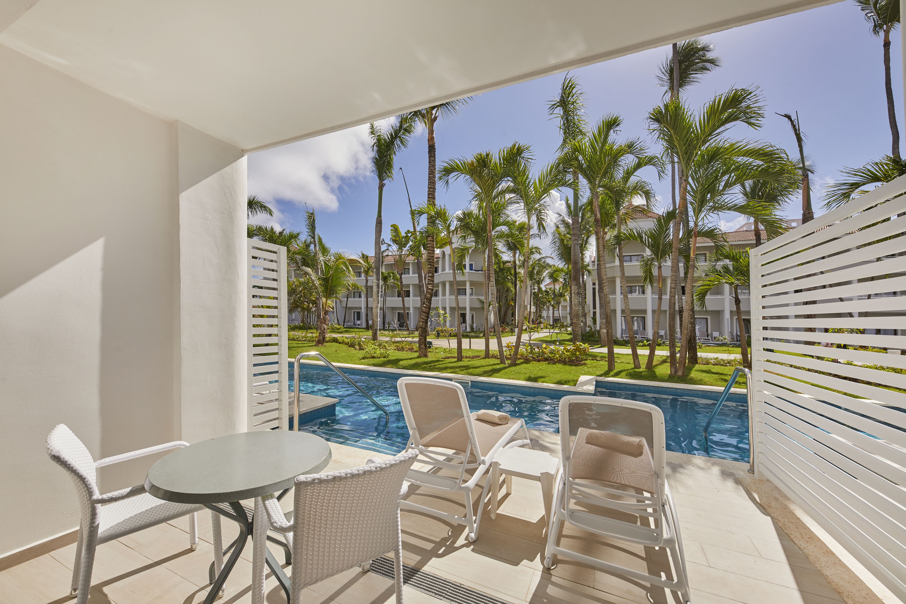 A balcony with a pool view, white furniture, and a clear sky.