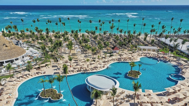 Un complexe hôtelier doté de plusieurs piscines, de palmiers et offrant une vue sur l’océan.