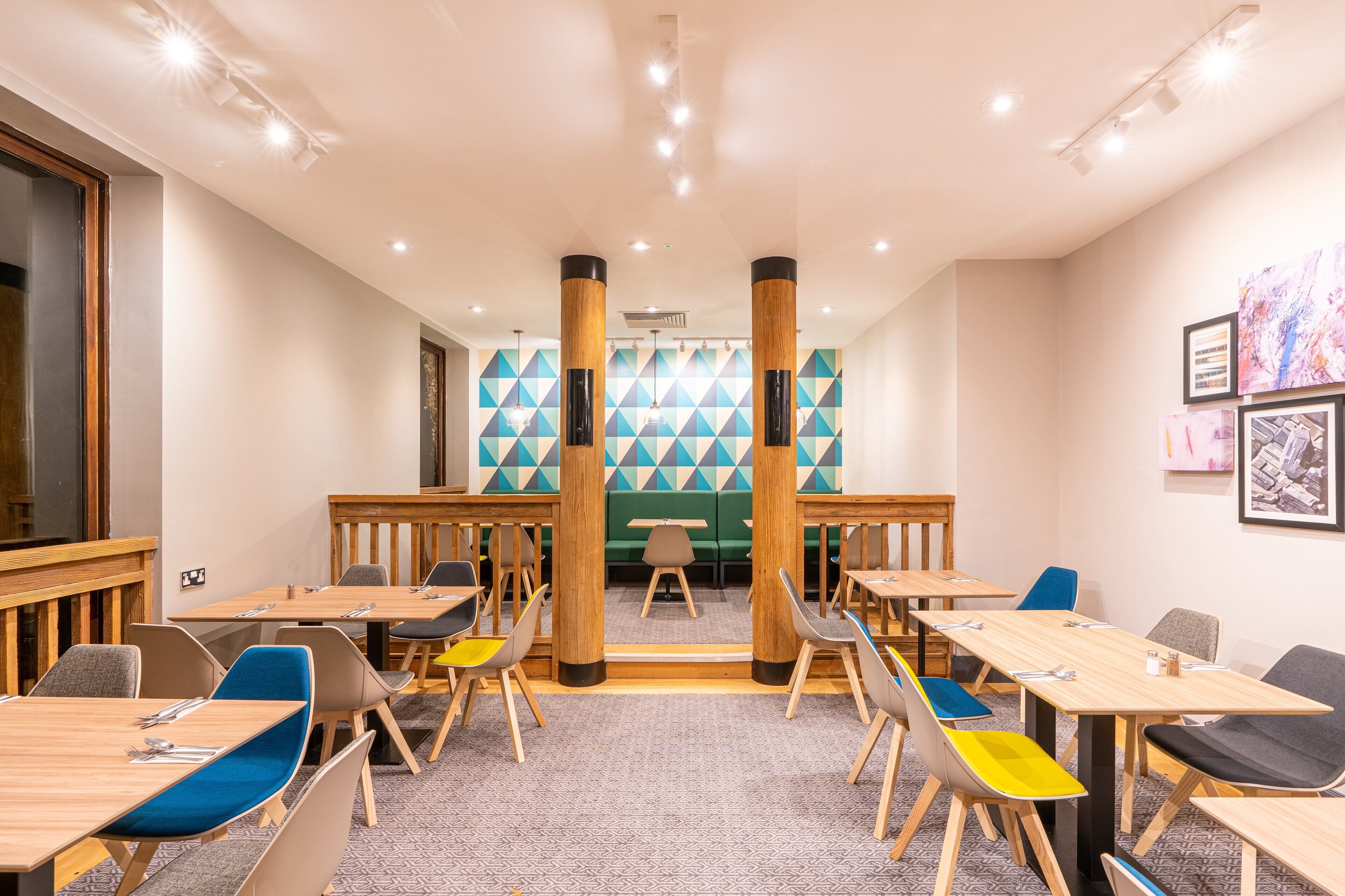A modern dining area with wooden tables and chairs, a patterned wall, and ceiling lights.