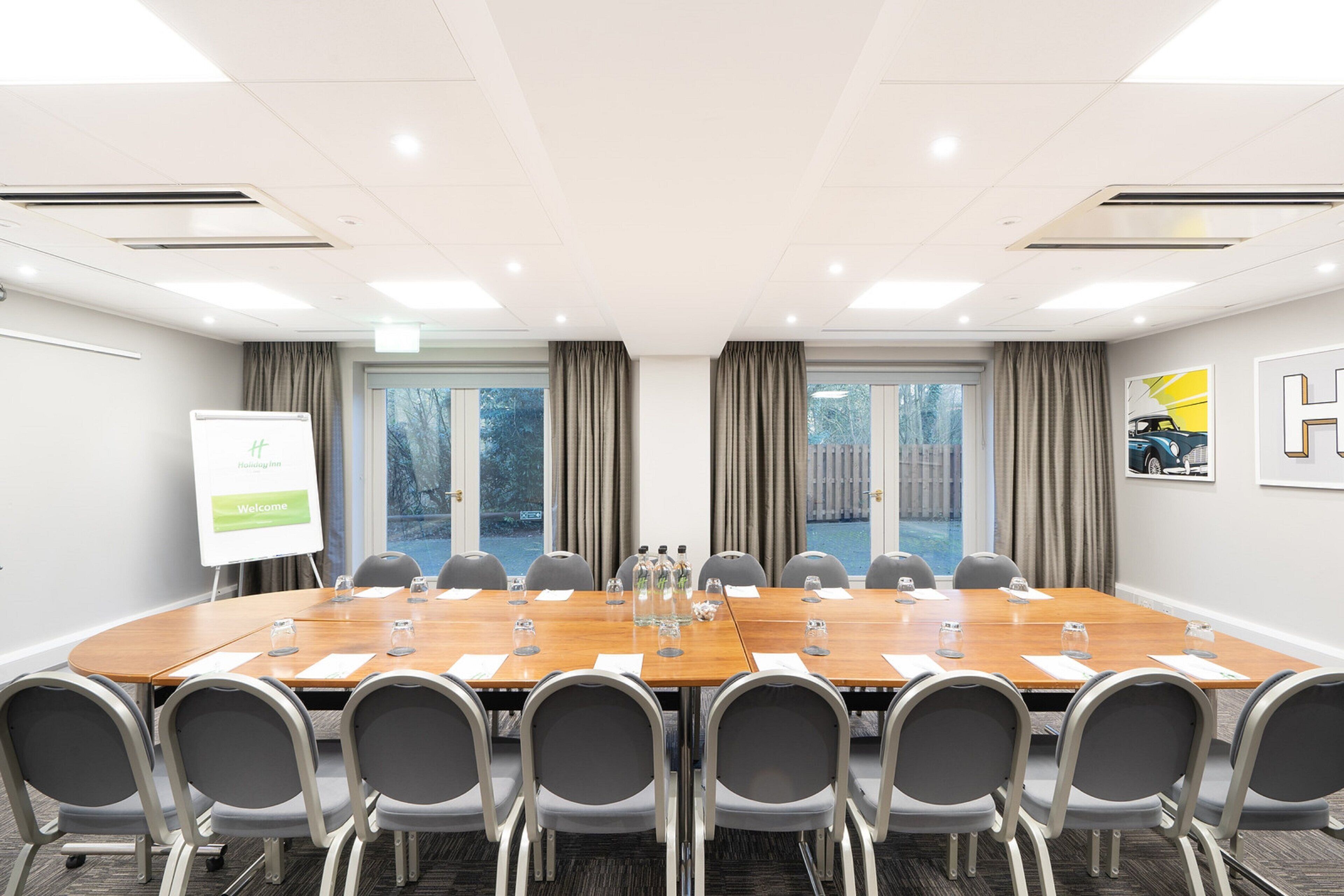 Un salón de conferencias con una larga mesa, sillas, una pizarra blanca y una ventana con cortinas.