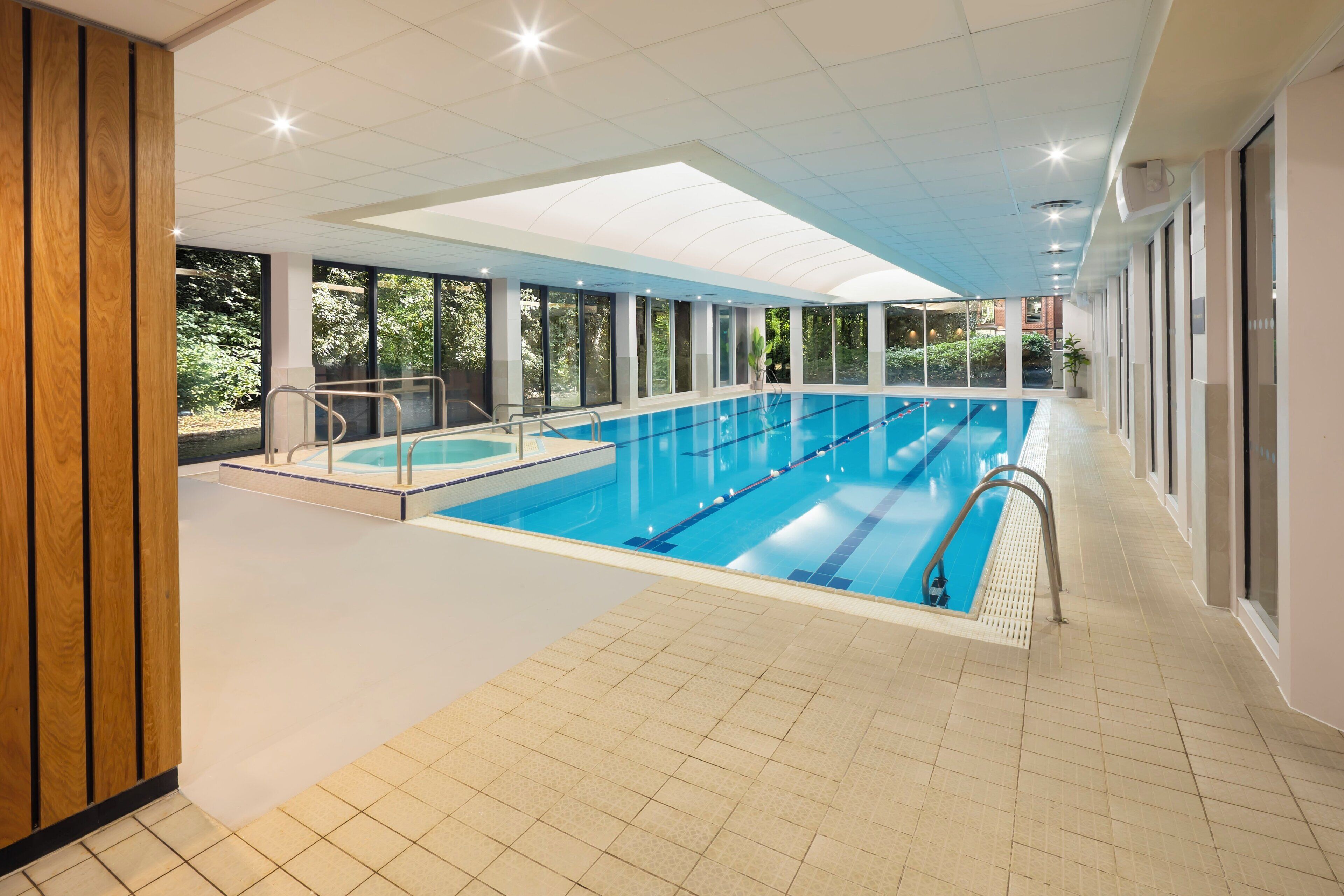 An indoor swimming pool with clear glass walls, a tiled floor, and a sunlit ceiling.