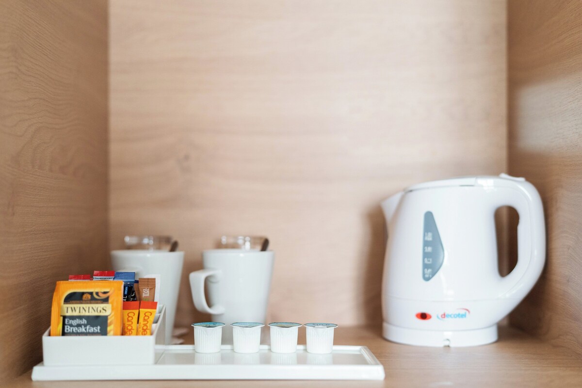 A white tray with coffee pods, a white mug, and a white electric kettle on a wooden surface.