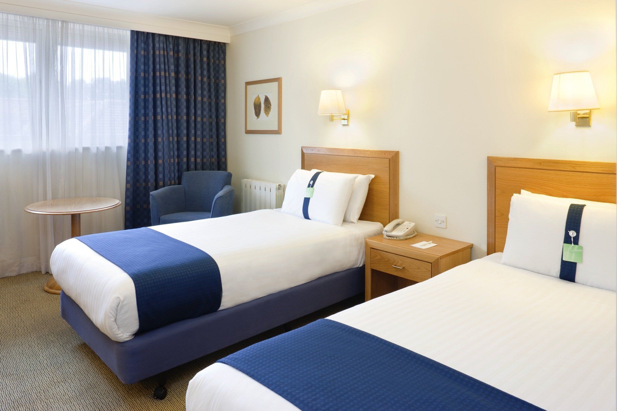 Habitación de hotel con dos camas, una silla, una mesita de noche con teléfono y una pequeña mesa redonda.
