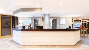 A hotel reception desk with a digital screen, a guest room tariff sign, and a reception area with a large window.