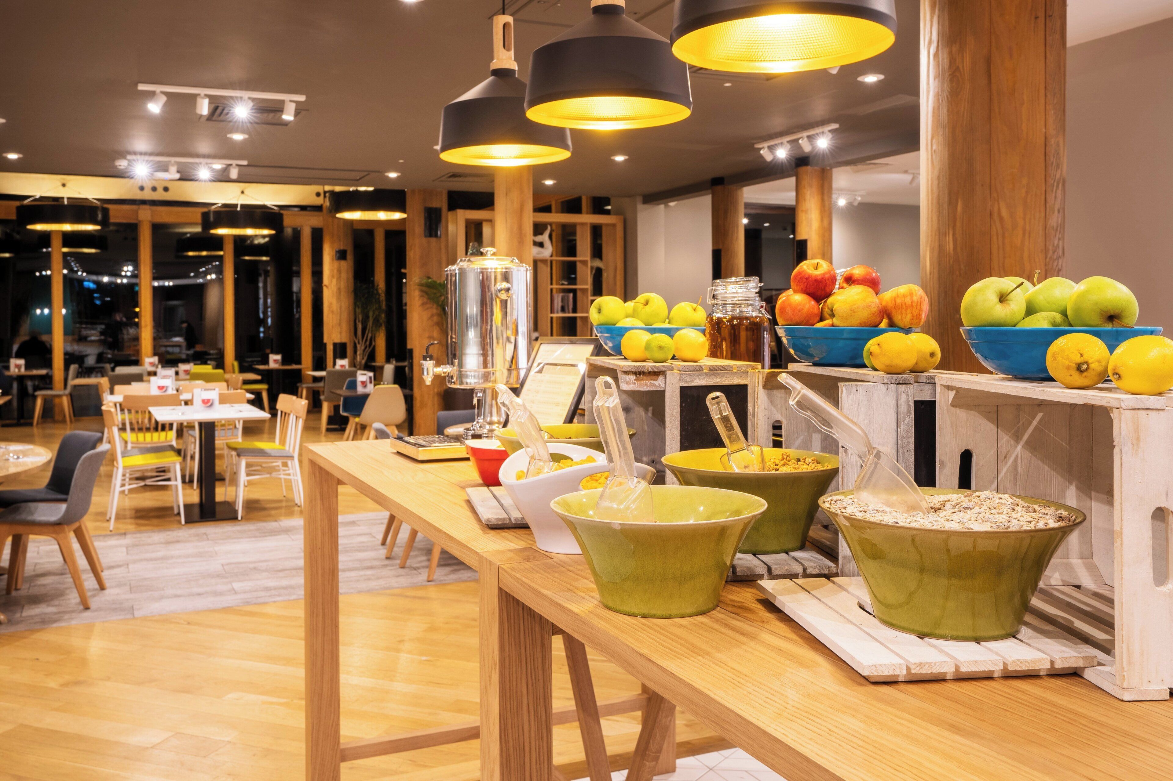 Interior de un restaurante con mesas de madera, lámparas colgantes y una exhibición de frutas.