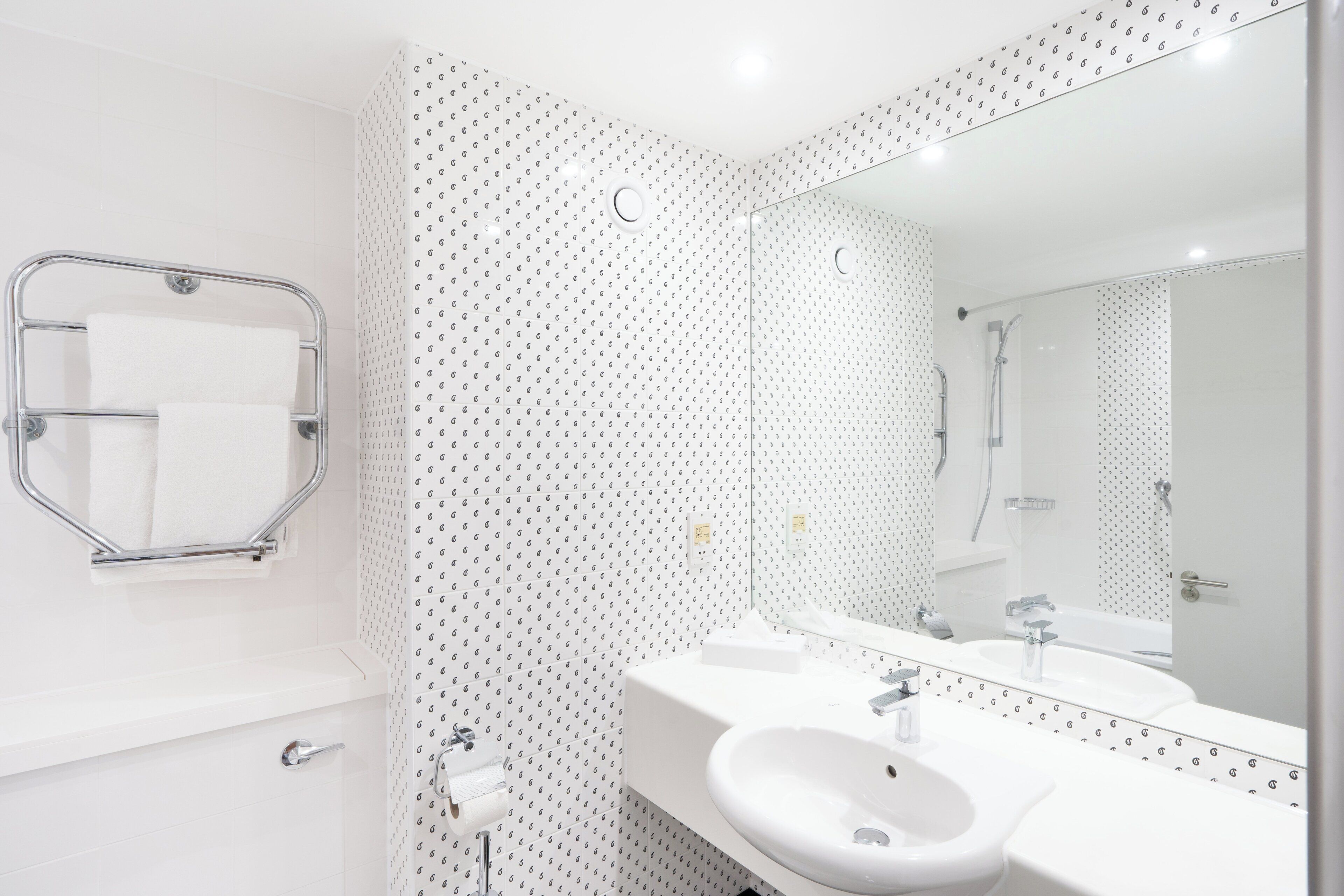 Un baño moderno con lavamanos, espejo y toallero blancos.