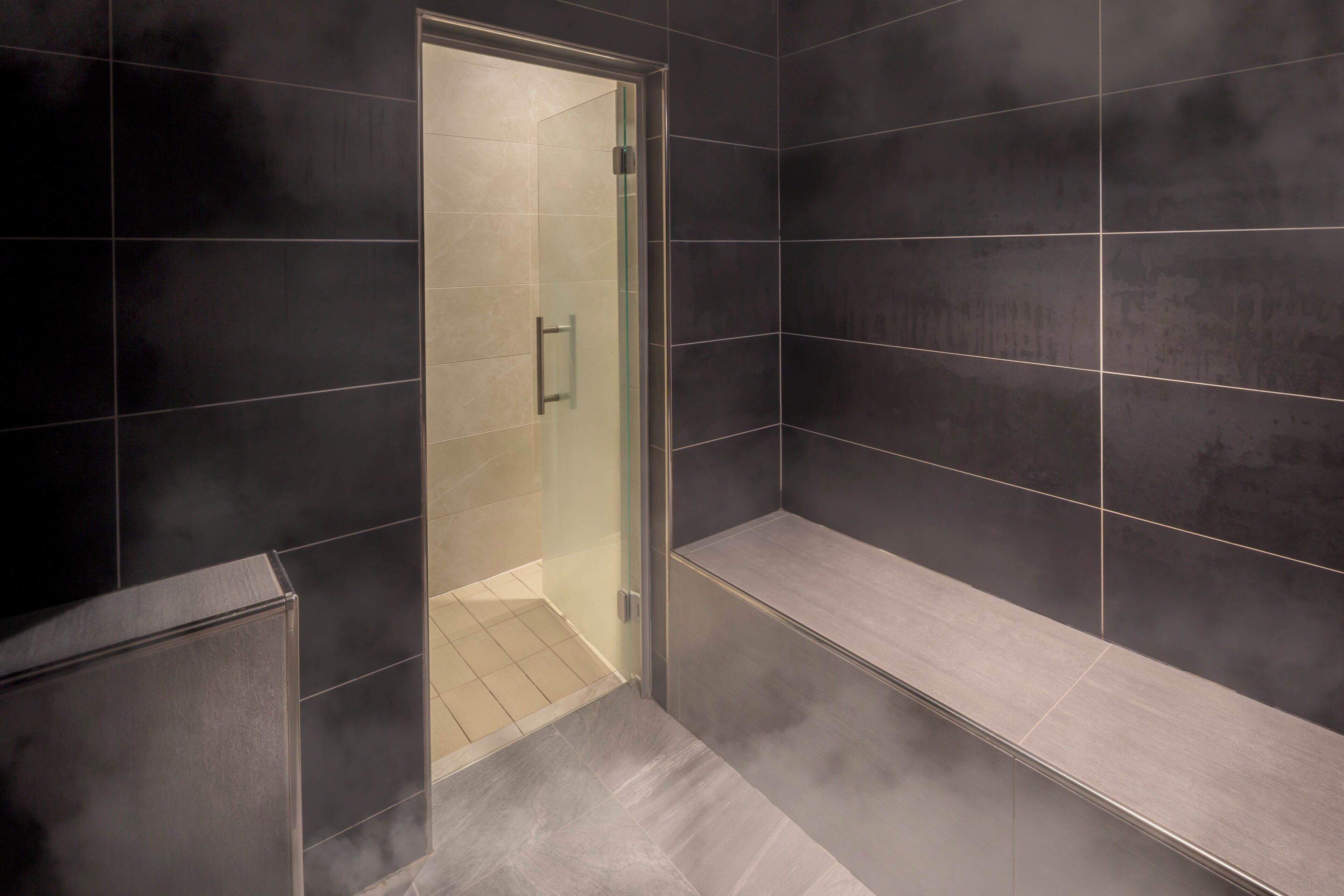 A modern bathroom with dark tiles, a glass shower enclosure, and a bench.