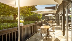 An outdoor patio with wooden decking, wicker chairs, and tables under large umbrellas. - Holiday Inn Hemel Hempstead M1, Jct. 8 by IHG (Hemel Hempstead)