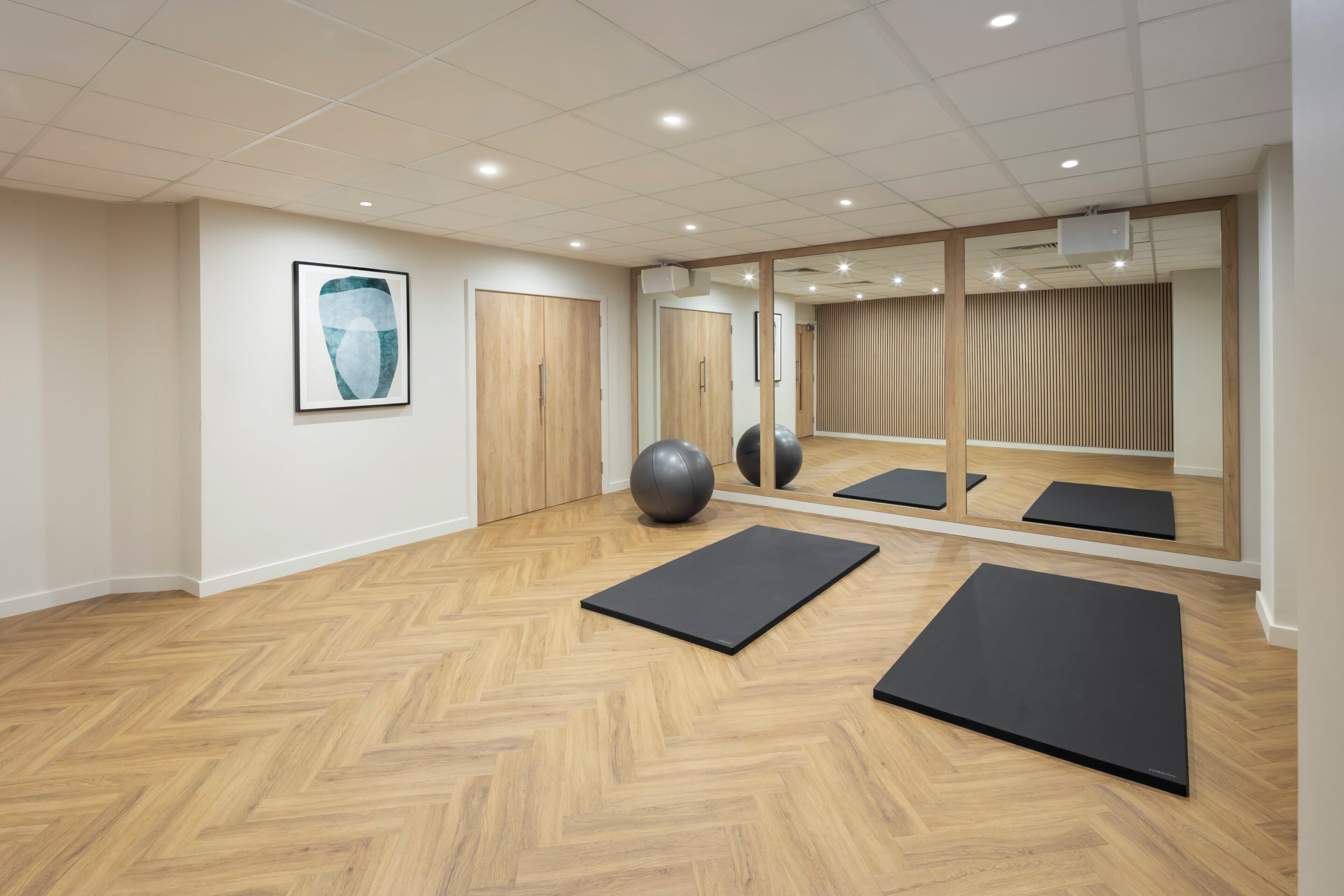 A room with wooden flooring, exercise mats, a large exercise ball, and a mirror reflecting the room.