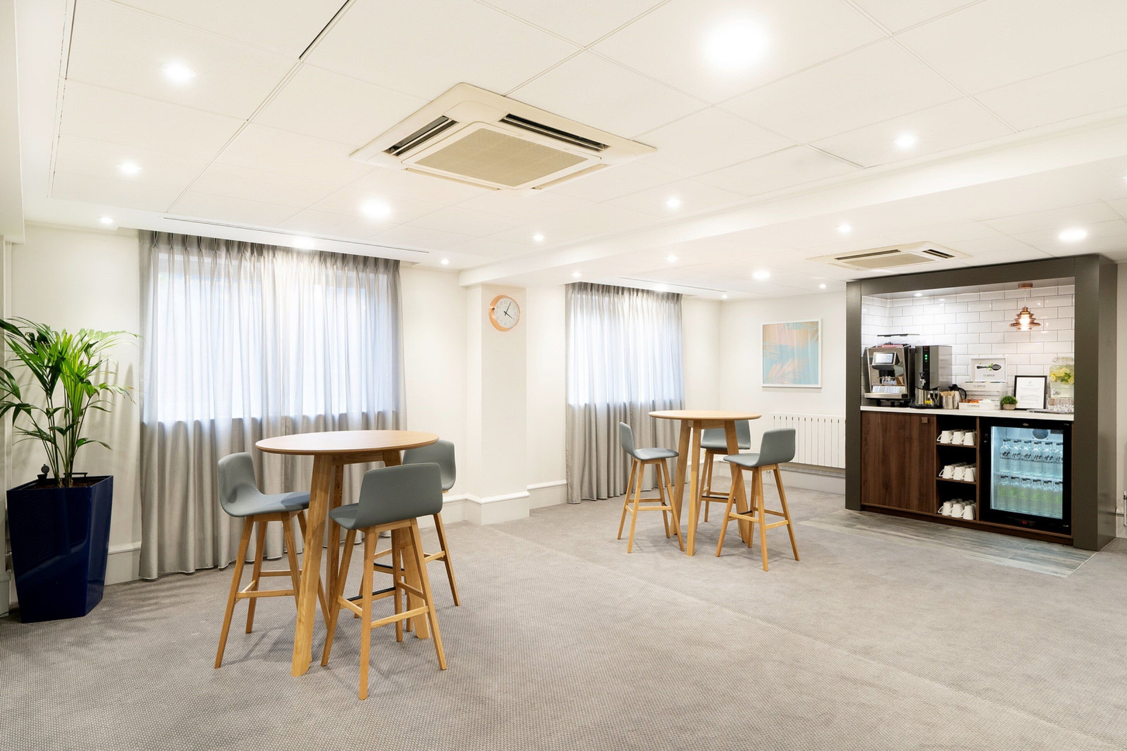 A modern hotel room with a dining area, a kitchen, and a large potted plant.