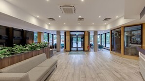 A modern reception area with a wooden reception desk, a seating area with a sofa, and large windows providing natural light. - Holiday Inn Hemel Hempstead M1, Jct. 8 by IHG (Hemel Hempstead)