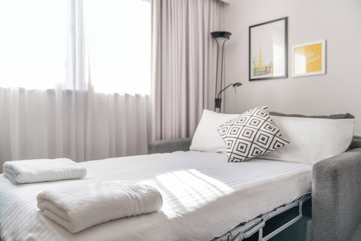 A neatly made bed with white linens and a folded towel, a bedside lamp, and two framed pictures on the wall.