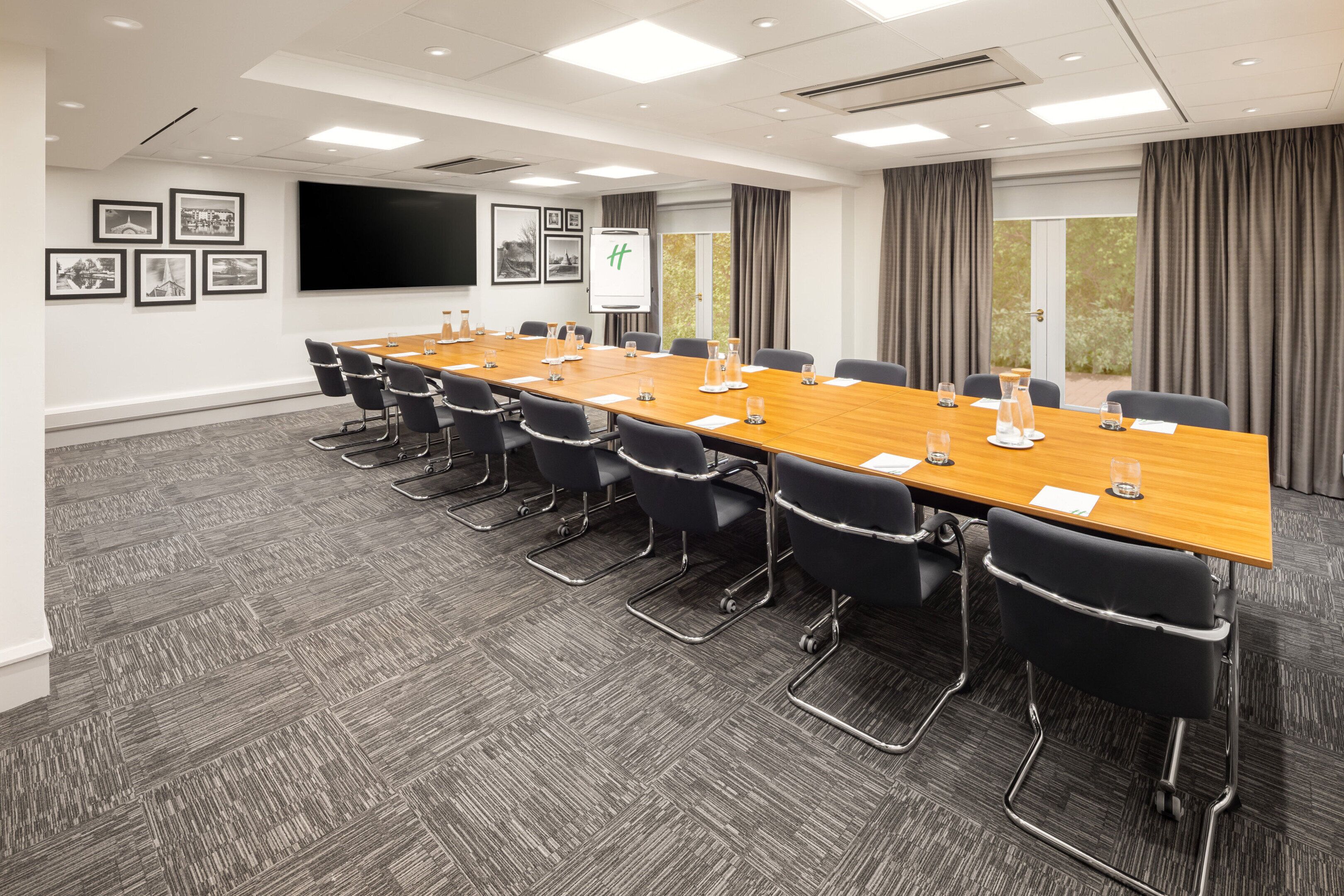 Une salle de conférence avec une longue table, des chaises noires, un tableau blanc et des tableaux encadrés accrochés au mur.