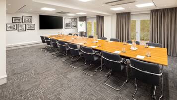 Une salle de conférence avec une longue table, des chaises noires, un tableau blanc et des tableaux encadrés accrochés au mur.