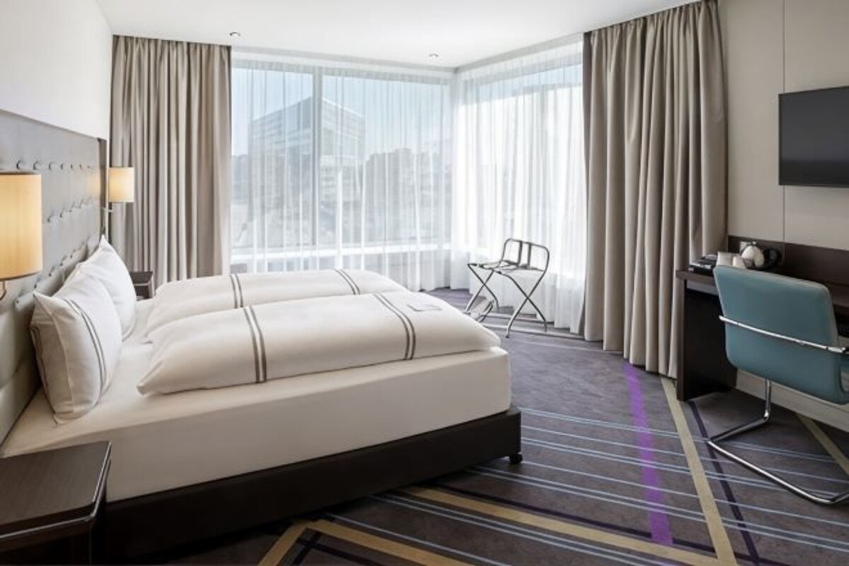 A hotel room with a large bed, a desk, a chair, and a TV.