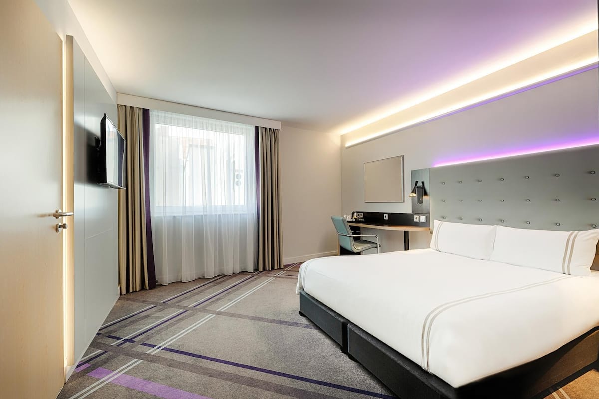 Une chambre d’hôtel avec un grand lit, un bureau, une chaise, une télévision et une fenêtre avec des rideaux.