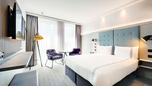A hotel room with a large bed, a desk, a chair, a TV, and a window with curtains.
