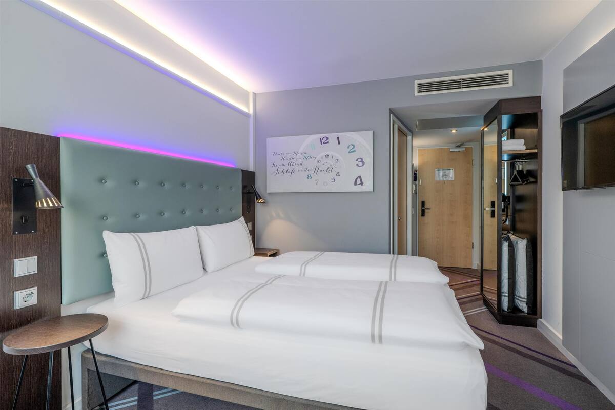 Une chambre d’hôtel moderne avec un grand lit, une table de chevet, une horloge murale, un miroir et un téléviseur.