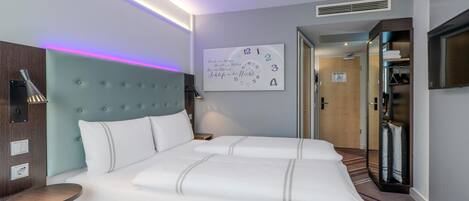 A modern hotel room with a large bed, a bedside table, a wall clock, a mirror, and a TV.