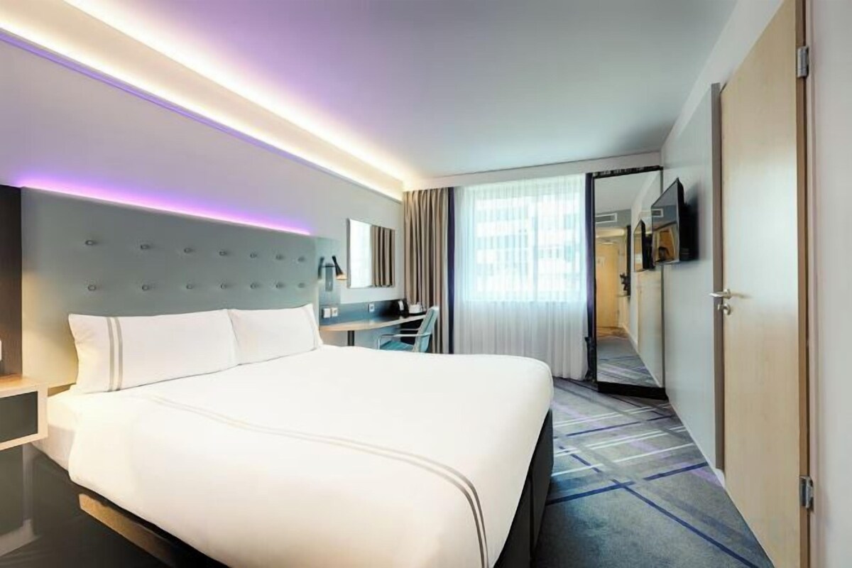 A hotel room with a large bed, a desk, a chair, and a mirror.