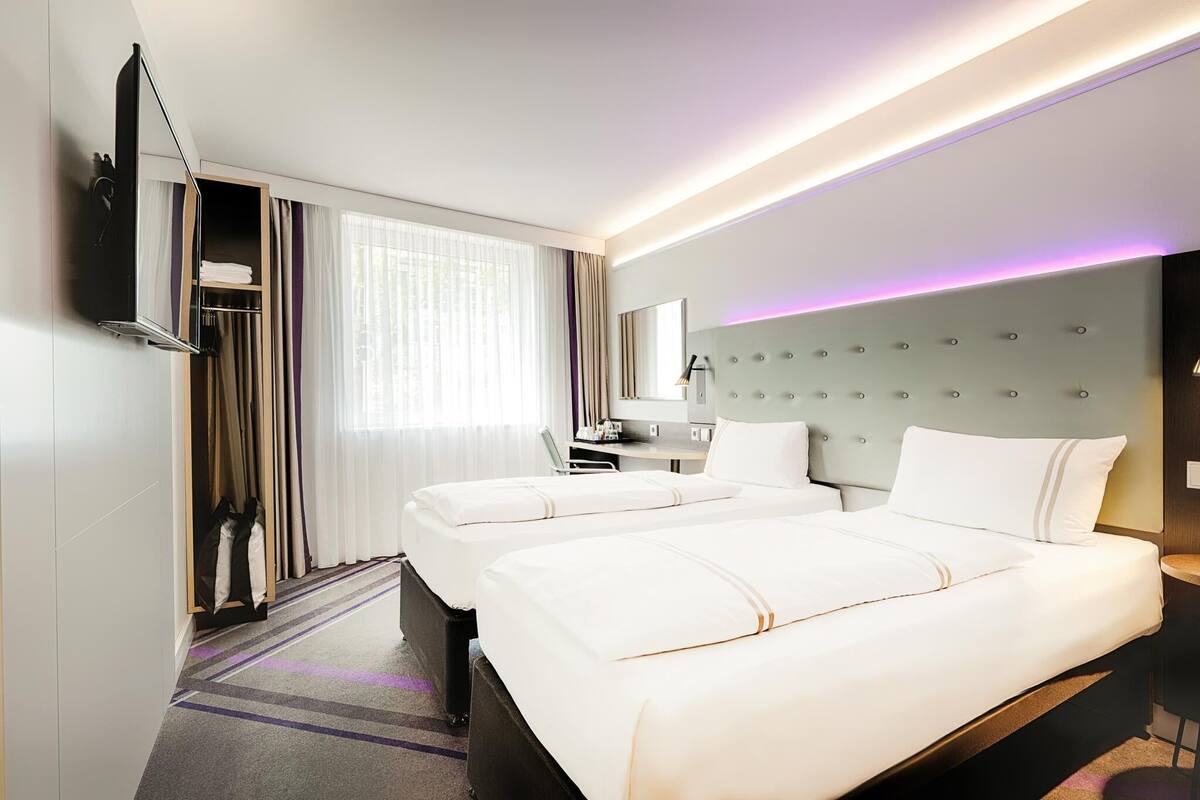 Une chambre d’hôtel avec deux lits, un bureau, une chaise, une télévision et une armoire.