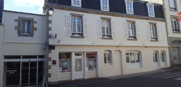 A hotel with a reception area, multiple windows with shutters, and a garage entrance. - Hôtel du Cheval Blanc (Saint-Pol-de-Leon)