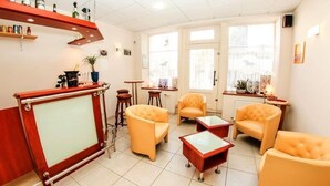 Un área de recepción con un escritorio de madera, varios sillones y una mesa baja. Se observan estantes con botellas y una planta en maceta.