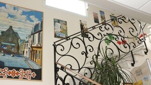 Una habitación con un cuadro grande que muestra una escena urbana, una escalera de hierro forjado negro y una planta en maceta.