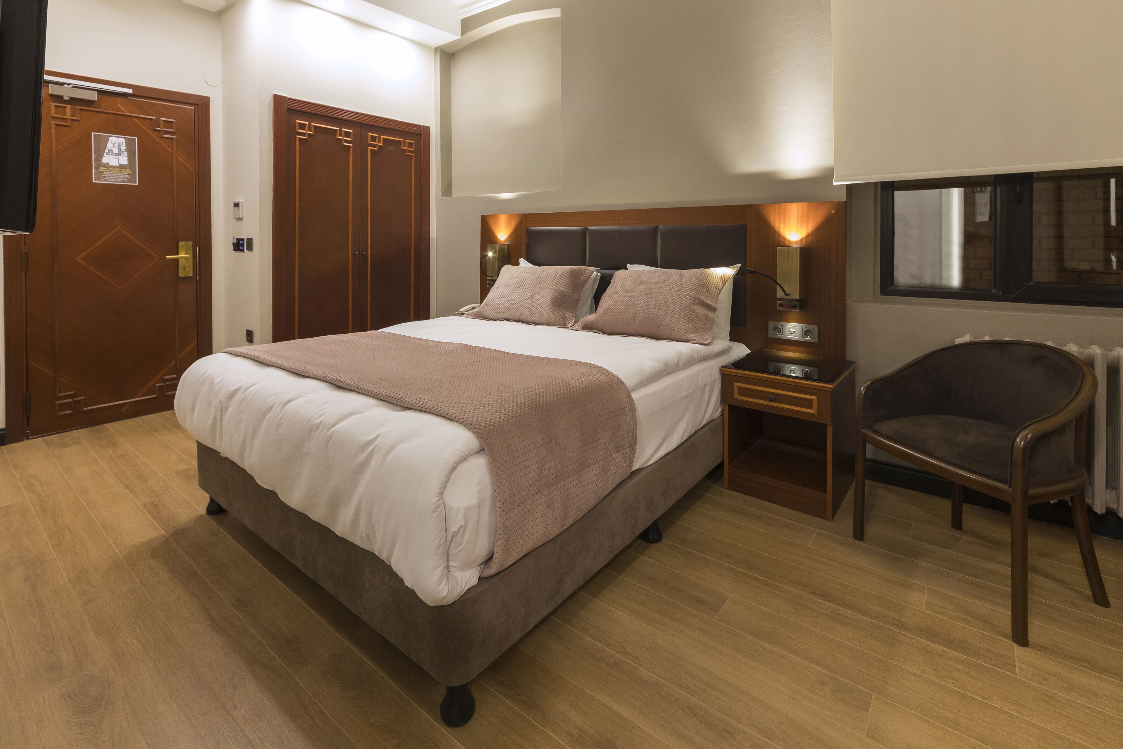 Una habitación de hotel con una cama grande, una mesita de noche, una silla y un ventanal.