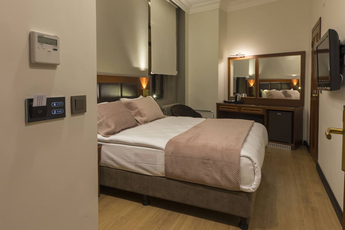 A hotel room with a bed, bedside table, mirror, and thermostat.