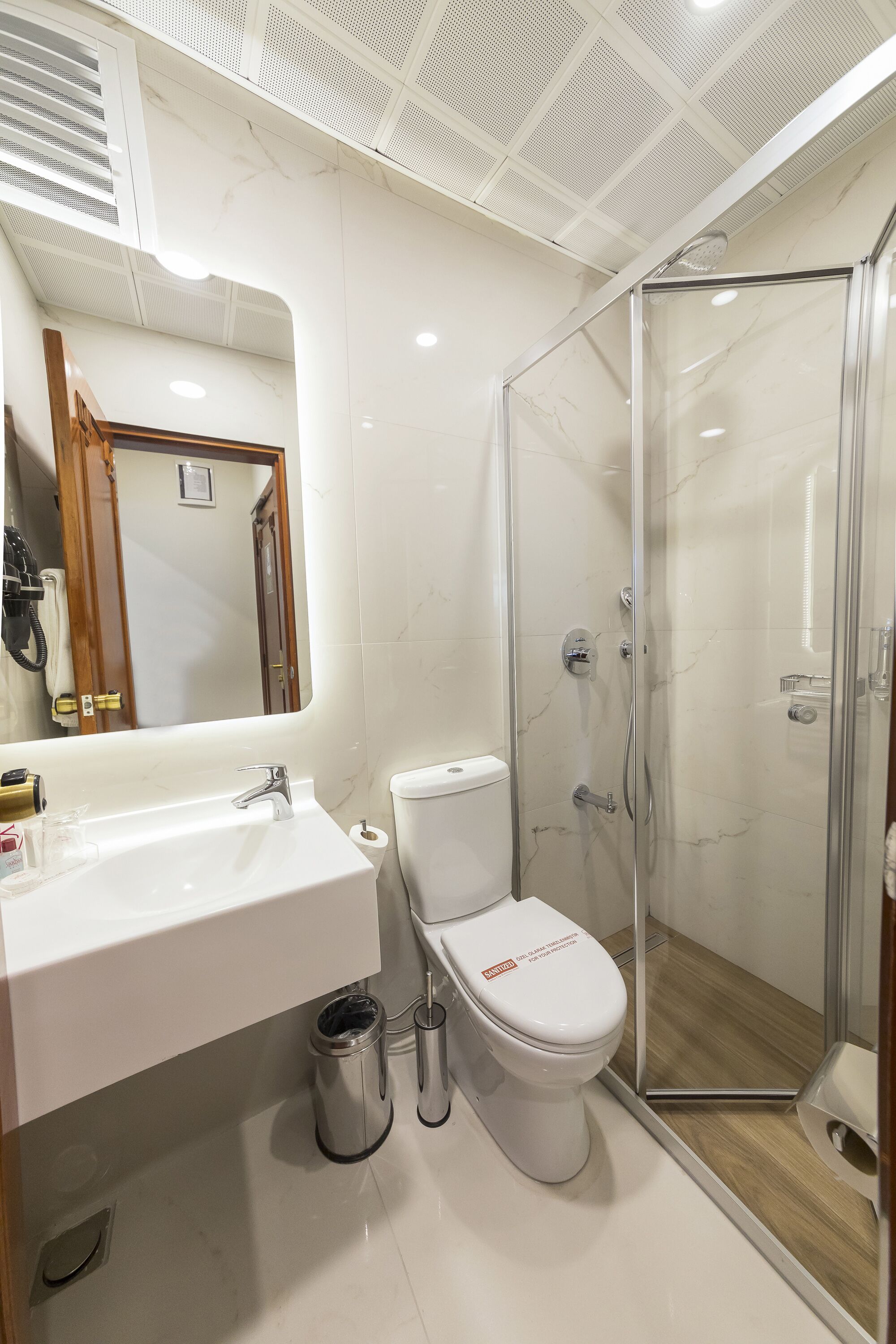 Een moderne badkamer met een douchecabine van glas, een witte wastafel met spiegel en een toilet.