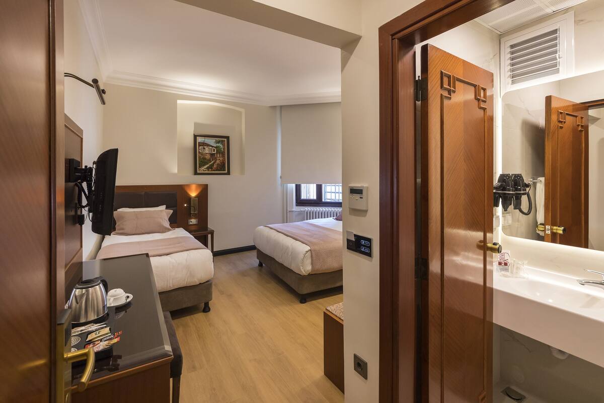 A hotel room with two beds, a desk with a coffee maker, and a bathroom with a sink and mirror.