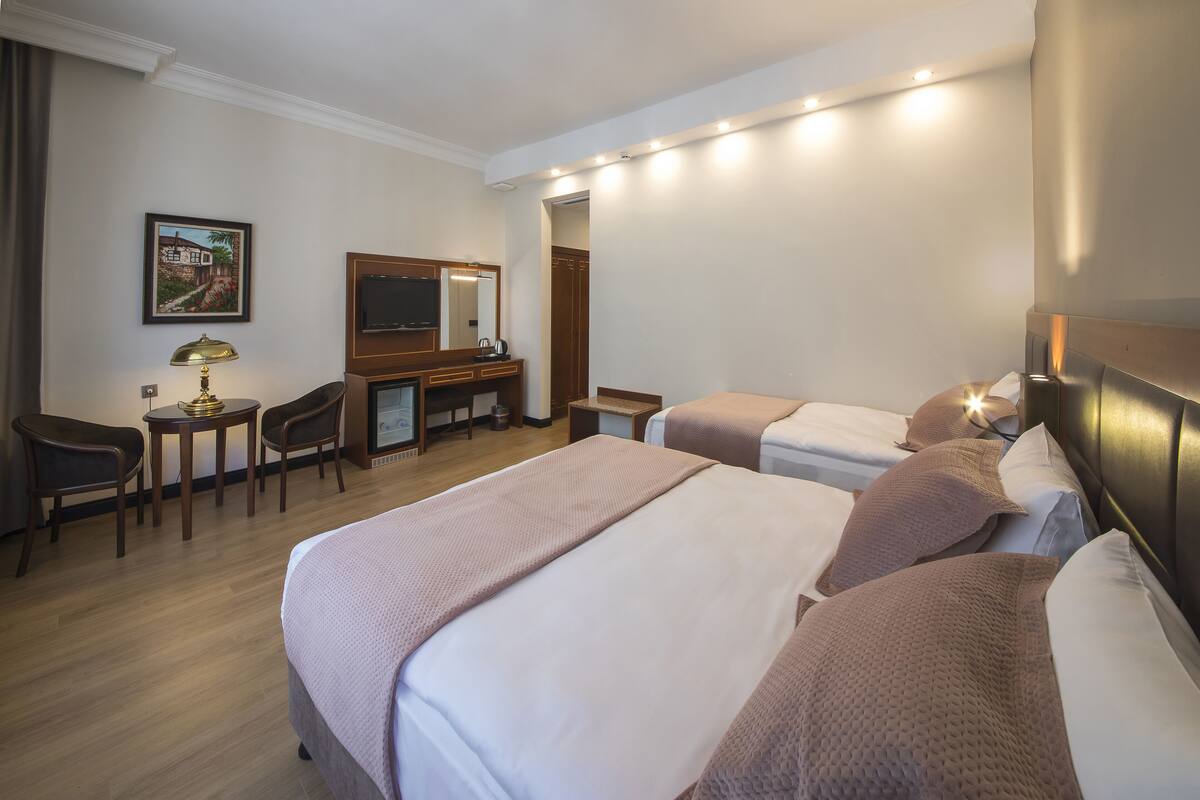 A hotel room with two beds, a desk with a chair, a TV, and a painting on the wall.