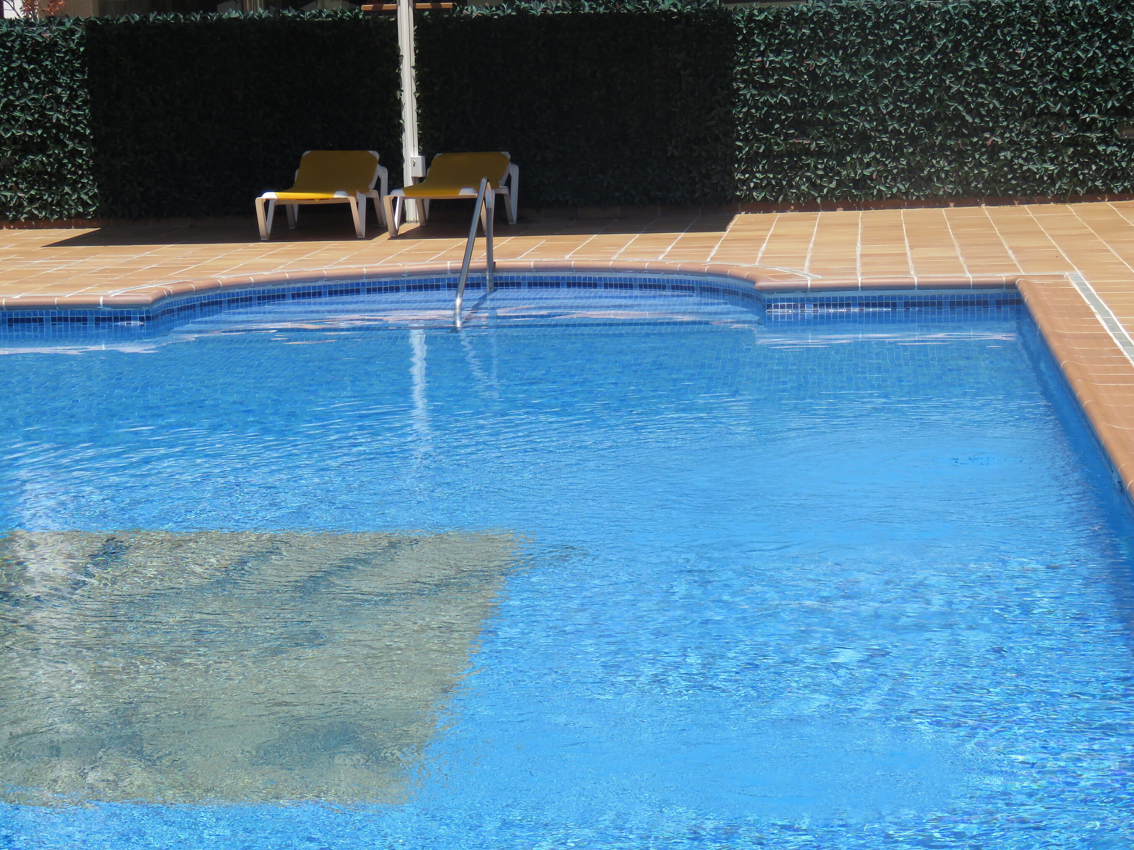 A swimming pool with clear blue water, surrounded by a tiled deck and two yellow lounge chairs.