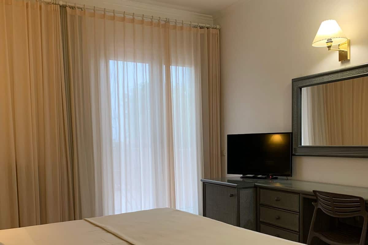 A hotel room with a bed, a desk with a television, a chair, and a large window with curtains.