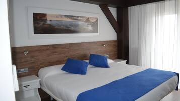 Habitación de hotel con una cama grande, dos almohadas azules, un cabecero blanco, una pared de acento de madera, un cuadro enmarcado y una mesita de noche con un cajón.
