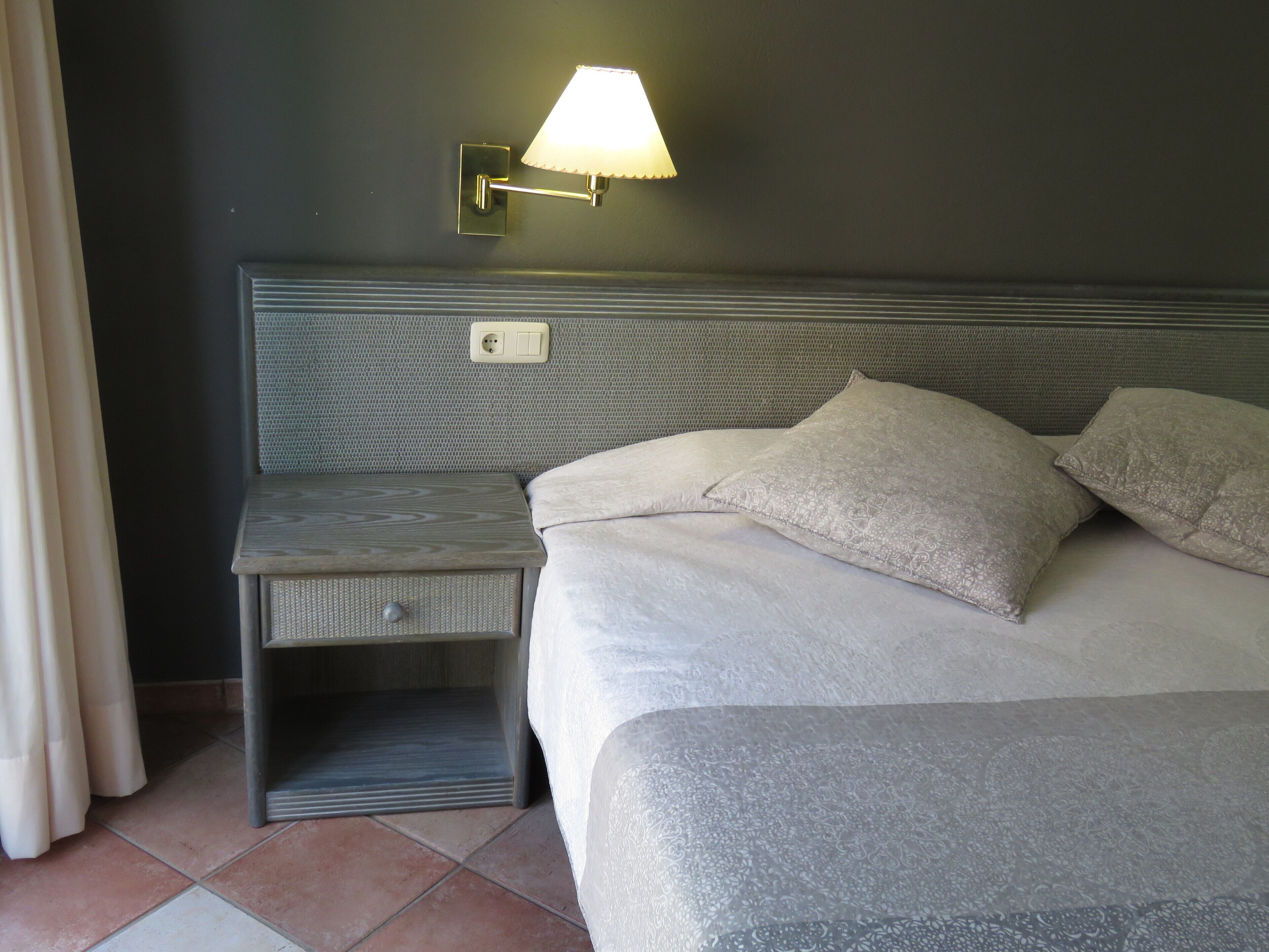 A neatly made bed with a headboard, a bedside table, and a wall-mounted lamp.