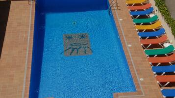 Una piscina rectangular con borde de azulejos, un adorno central con diseño de estrella de mar y una fila de sillas reclinables de colores a la derecha.