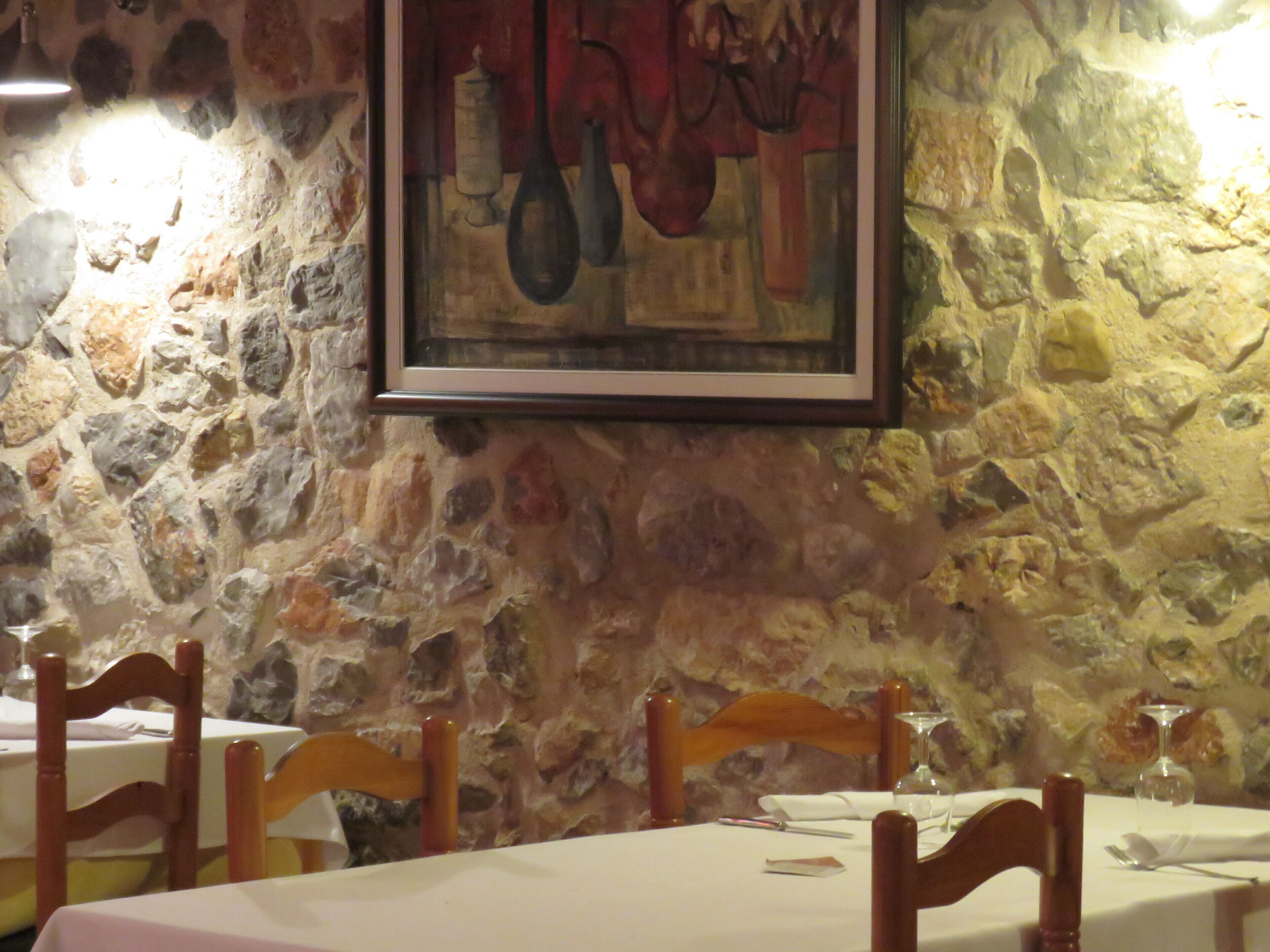 Un restaurant aux murs de pierre, aux chaises en bois et à la table dressée pour le repas.