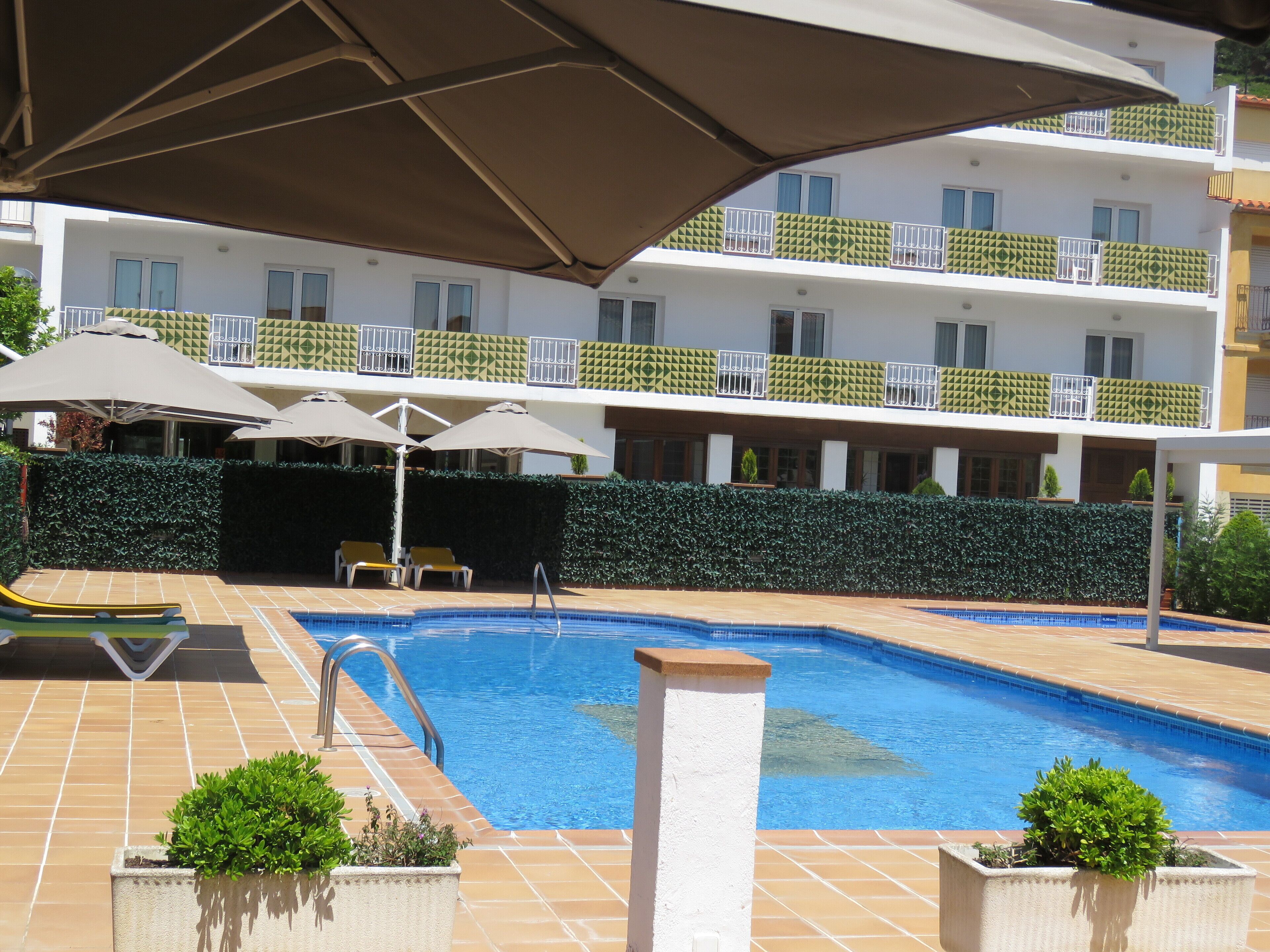 Une piscine dont le fond est recouvert de carrelage, entourée de chaises longues et de parasols.