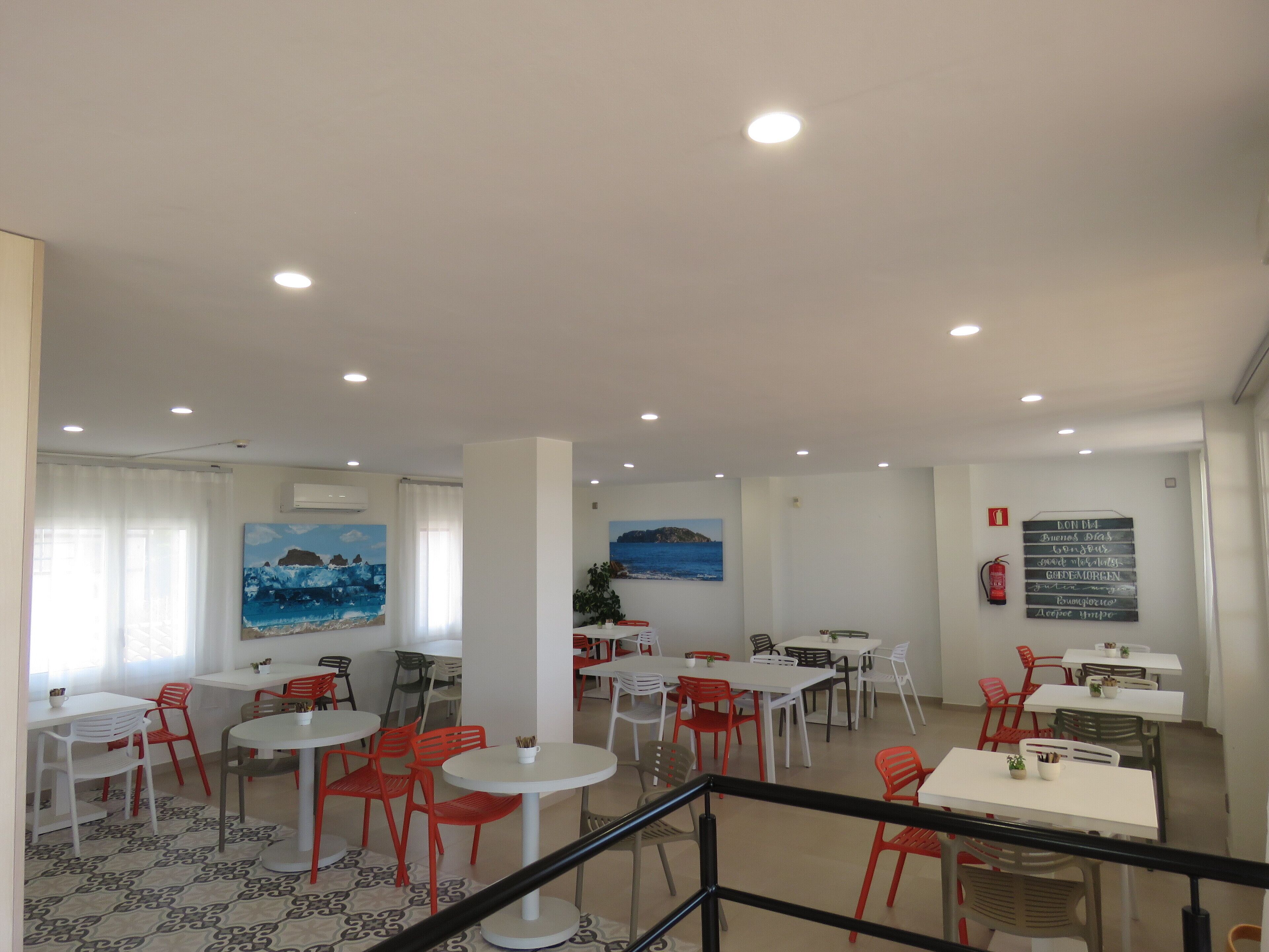 A dining area with tables and chairs, paintings on the walls, and a sign with text.