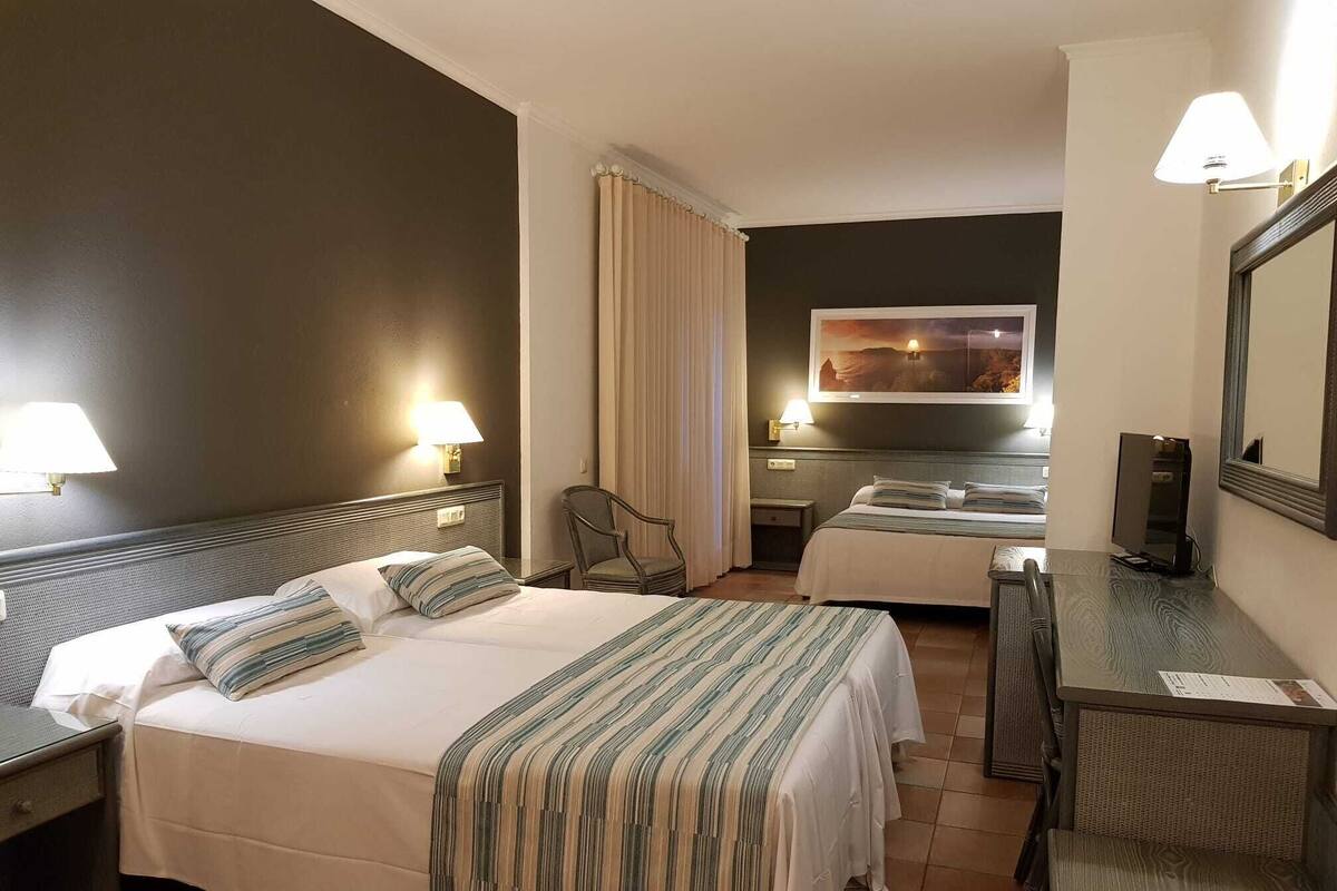 A hotel room with two beds, a desk, a chair, a mirror, and a painting on the wall.