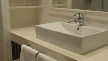Un baño con un lavabo blanco, un espejo encima y una toalla colgada en un perchero.