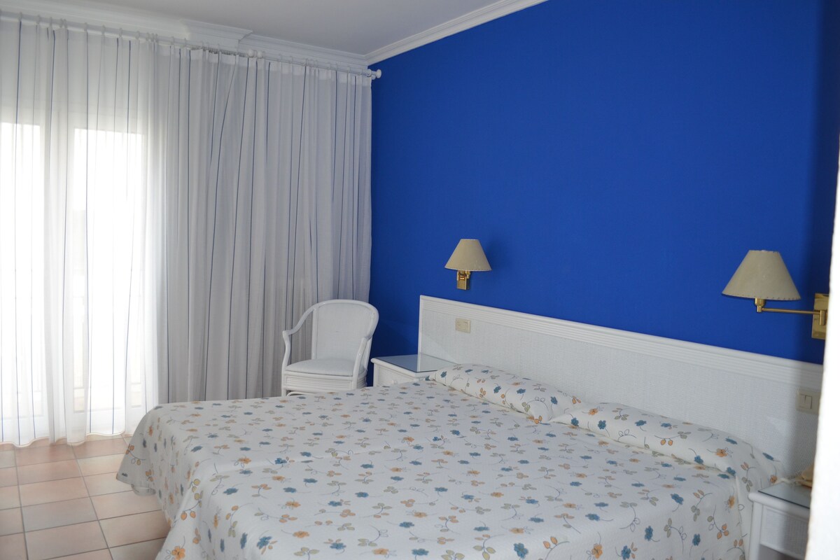 A bedroom with a bed, a chair, a nightstand, and a lamp.