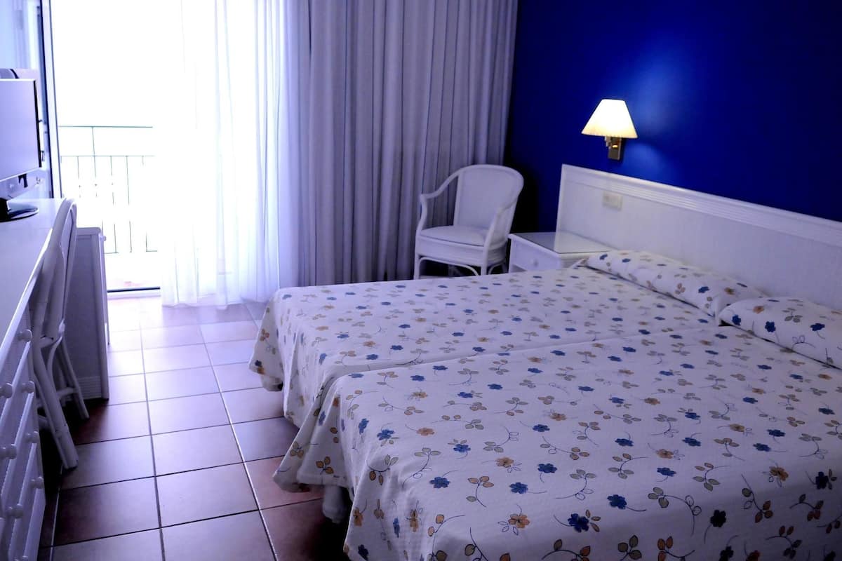 A hotel room with a bed, a chair, a desk, and a lamp.