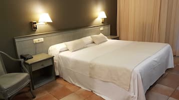 Een net opgemaakt bed met witte lakens, een nachtkastje met een lamp en een stoel.