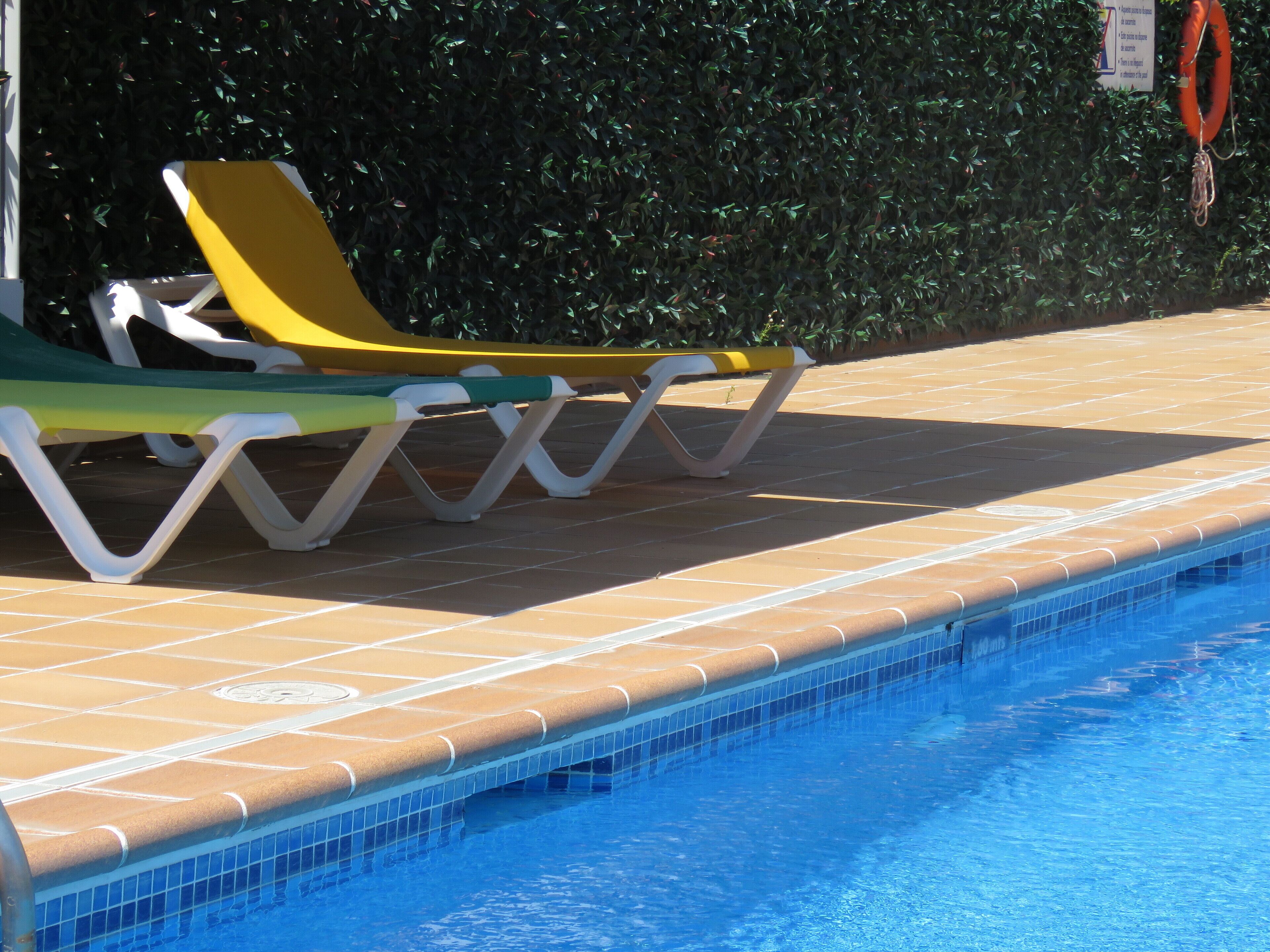 A swimming pool with tiled edges and lounge chairs.