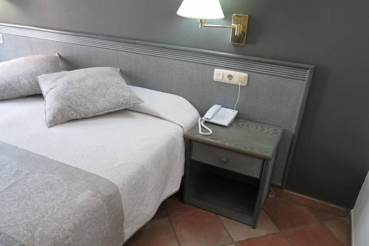 A hotel room with a bed, a bedside table with a lamp, and a phone.