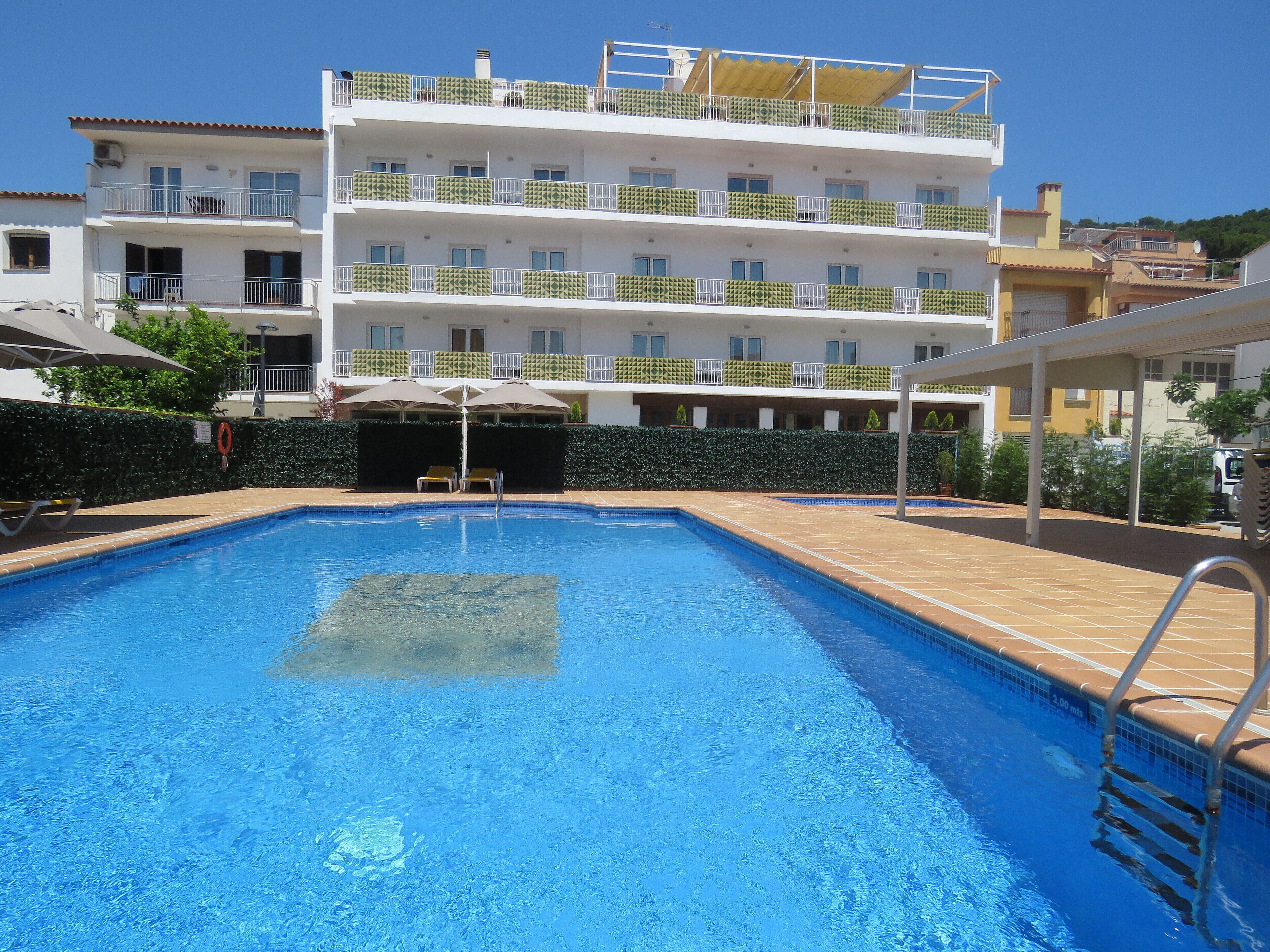Una piscina con bordo piastrellato, circondata da un edificio a più piani con balconi.
