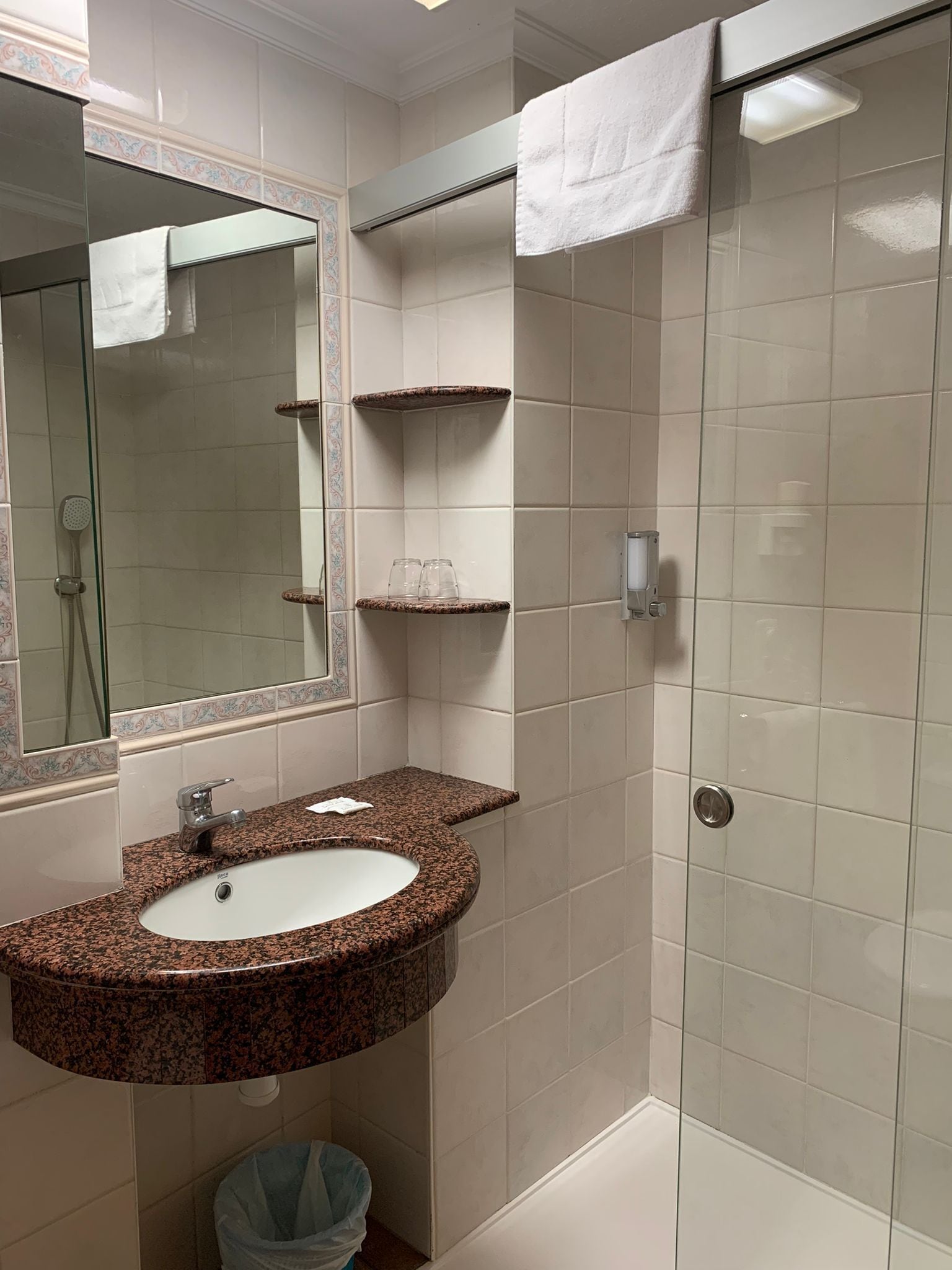 Un baño con lavamanos de granito, espejo, ducha y perchero para toallas.